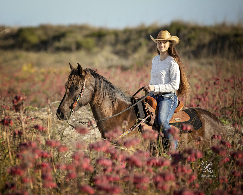 Girl riding horse in red flowers on beach taken a horse photography workshop