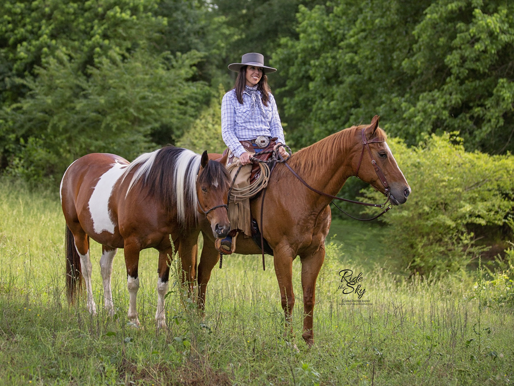 Cowgirl and two horses in green field