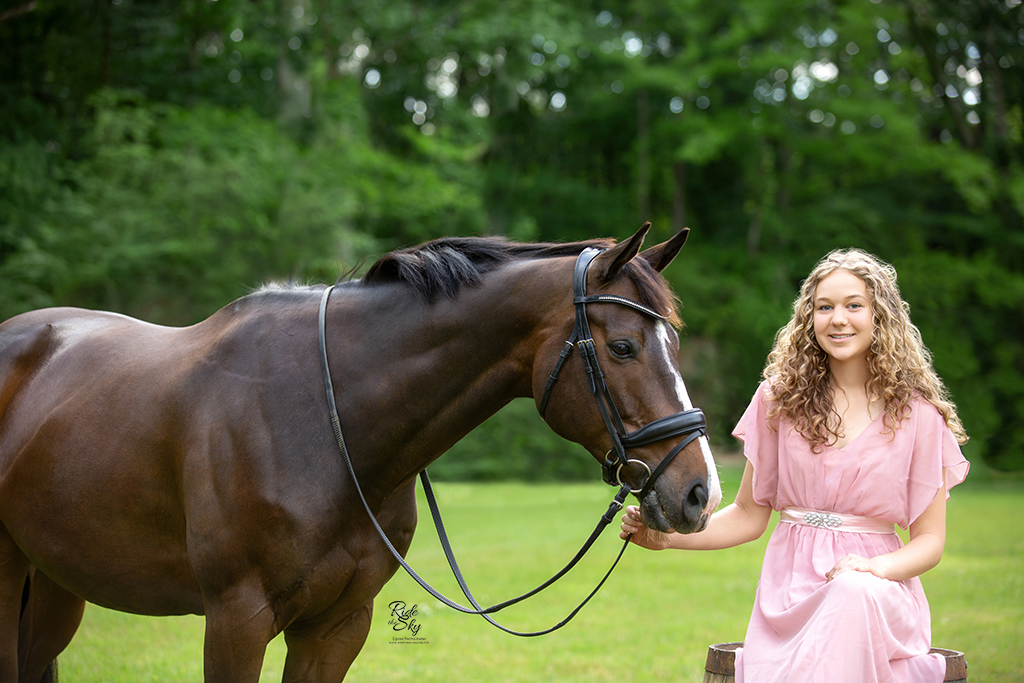 Girl on whiskey barrel in field with horse