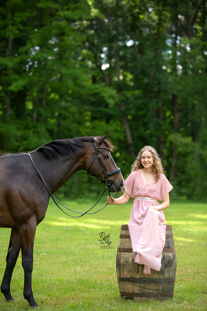 Girl in pink dress sitting on whiskey barrel next to horse