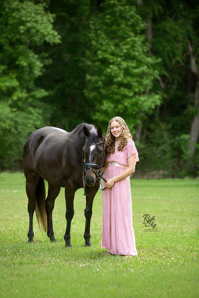 girl posed in pink dress with thoroughbred horse in field