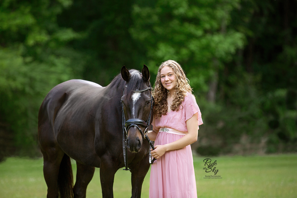 Girl in pink dress with thoroughbred horse in field