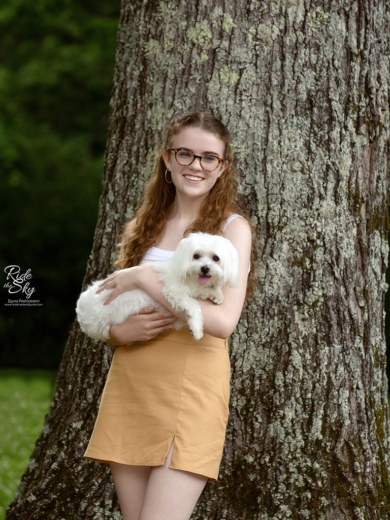 Girl leaning on tree holding dog