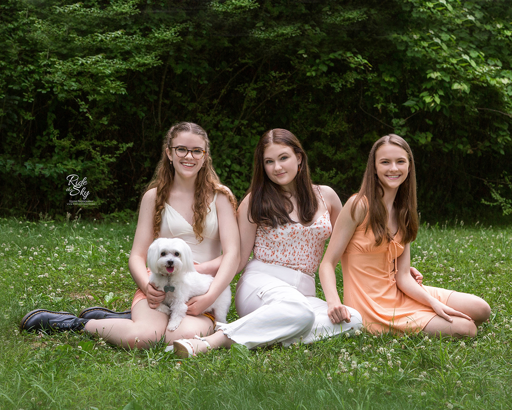 Three teenage girls sitting on ground in nature park in summer with white dog