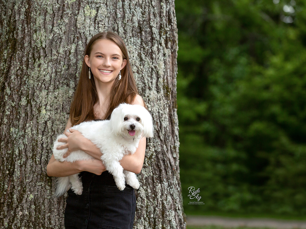 Girl leaning on tree holding white dog