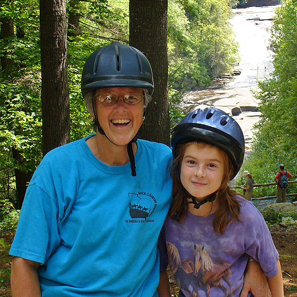 Woman with granddaughter wearing helmets on horse trail ride