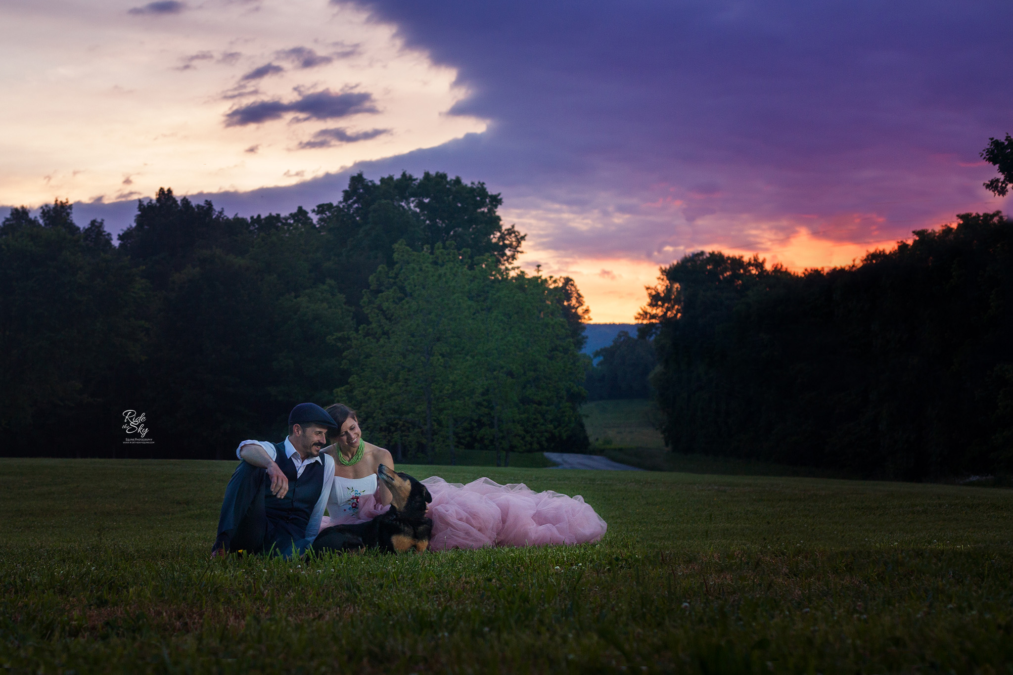 Woman in pink skirt and man in suit with dog in field at sunset