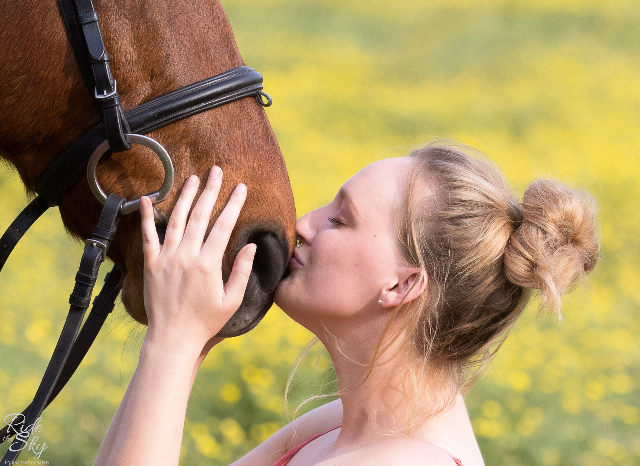 woman kissing horse muzzle in yellow flower field