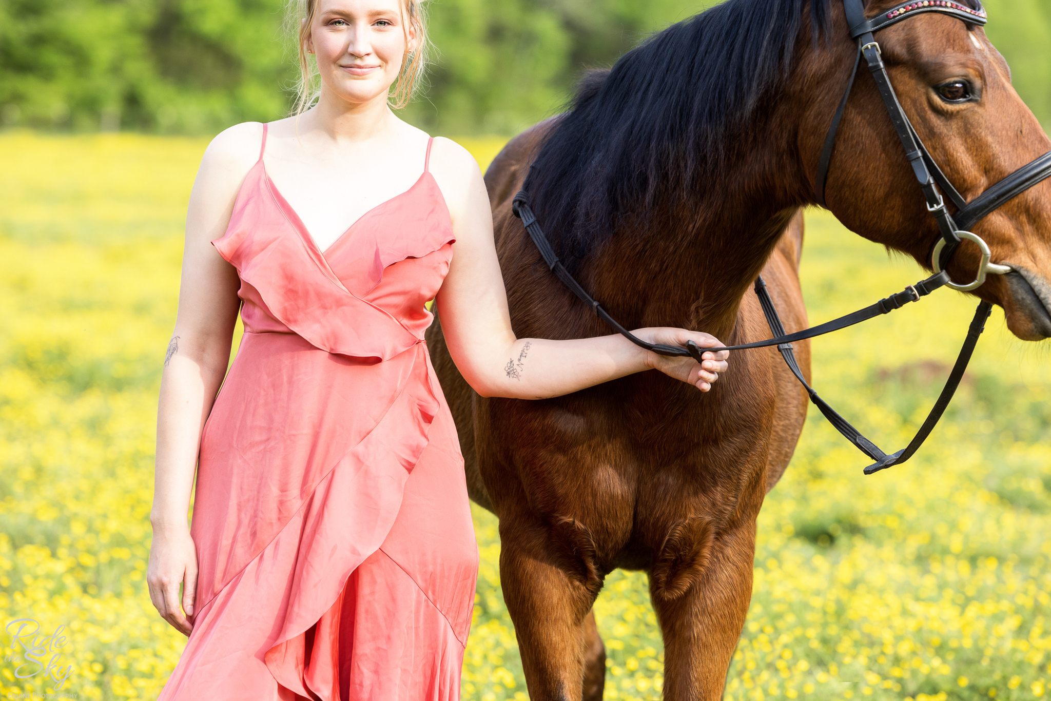 Woman in dress and horse in bridle standing in field of yellow flowers with tattoo of horse's kill pen number tattooed on arm