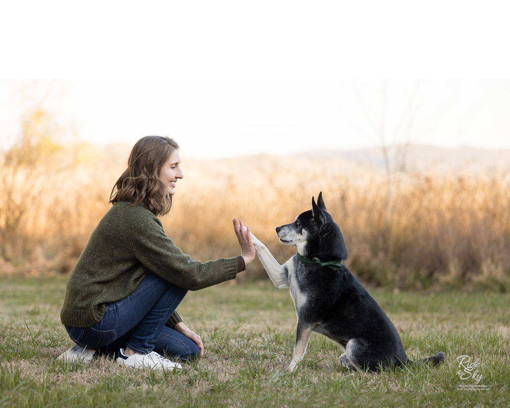 women with her dog doing a high five outside in a field